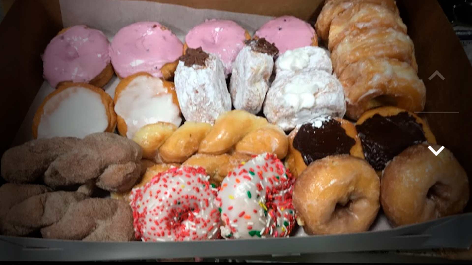 Caixa de papelão aberta com variedade de donuts glaceados, cobertos com granulado colorido, polvilhados com açúcar e com cobertura de chocolate